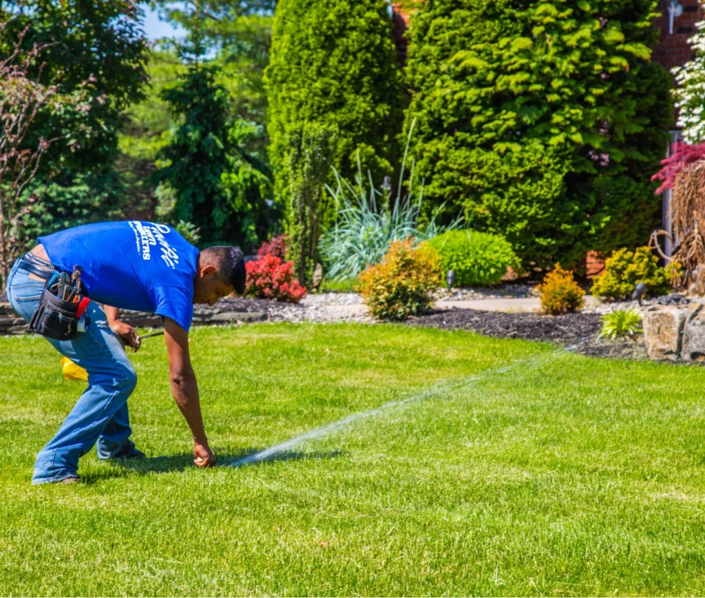 A lawn sprinkler technician adjusts a spraying sprinkler head on a green residential lawn.