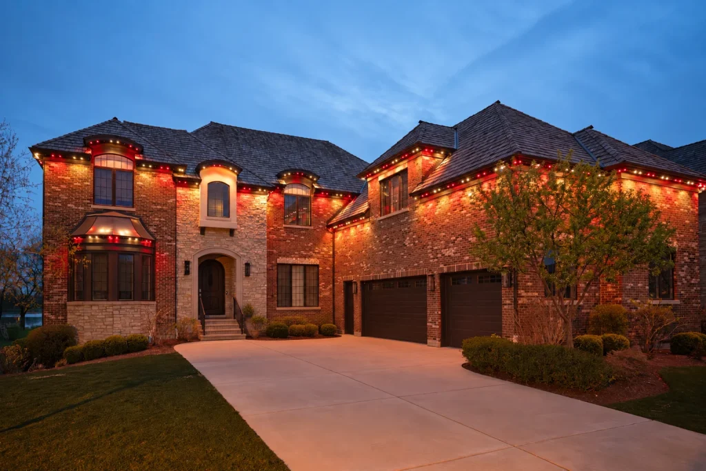 Upscale brick and stone home glowing with festive red lights under a blue evening sky.